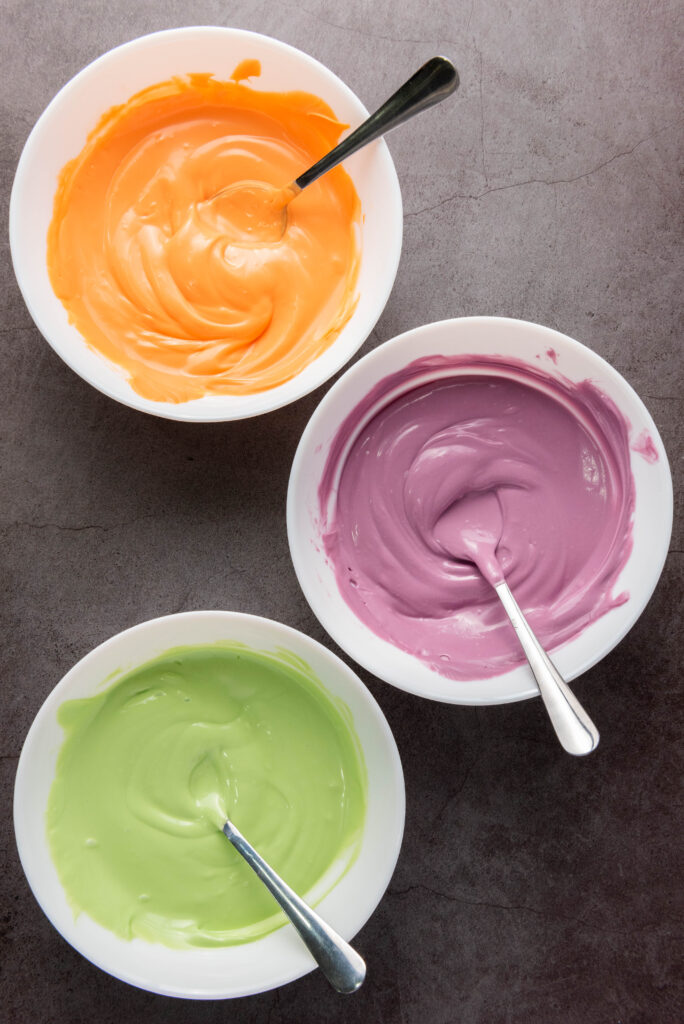 A picture of orange, purple, and green candy melted in separate bowls.