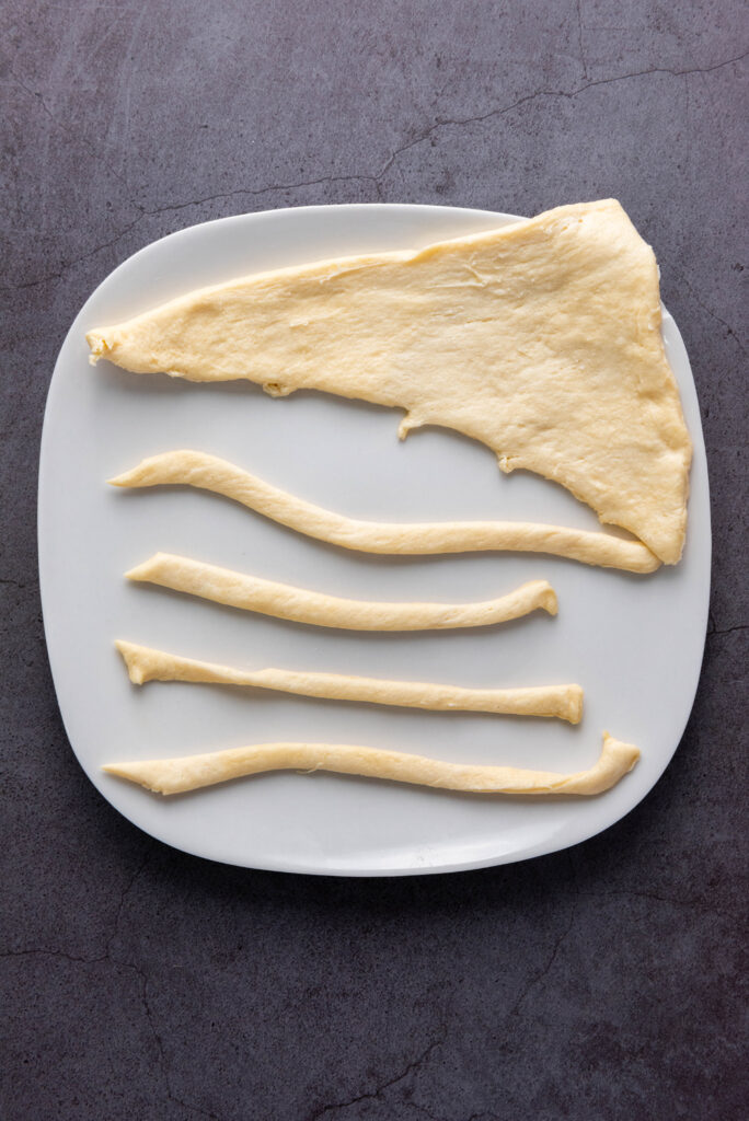 A picture of crescent roll dough rolled flat into a triangle, being cut into strips.