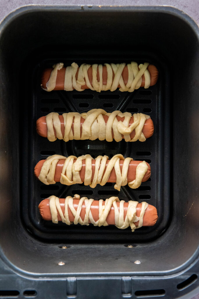 A picture of four crescent roll wrapped hot dogs in an air fryer basket.