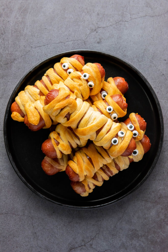 A picture of a plate of air fryer mummy dogs decorated with edible eyes.