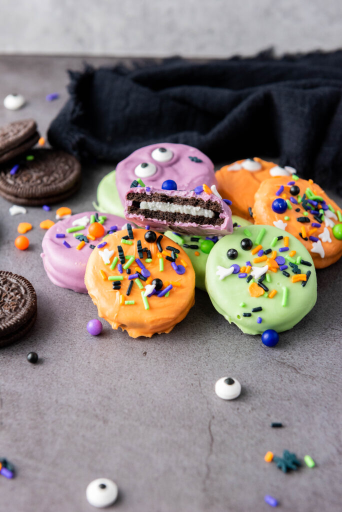 A picture of a small pile of candy dipped oreo cookies with a bite taken out of the cookie in the middle.