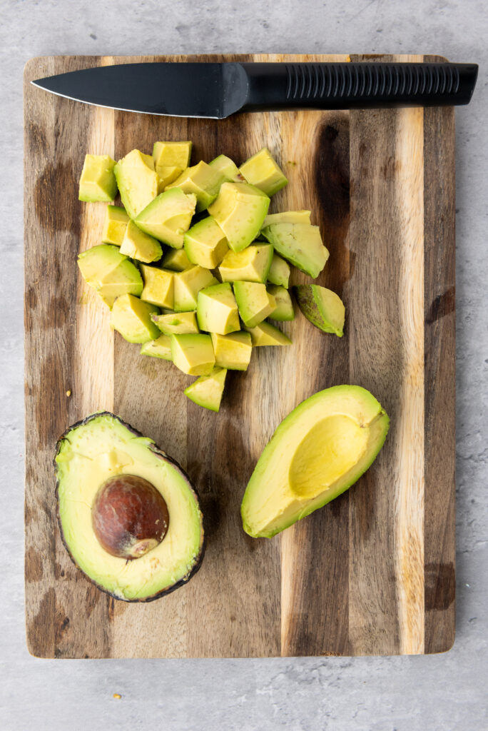 A picture of an avocado cut in half next to chunks of diced avocado.