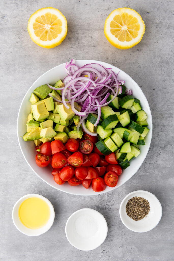 A picture of diced cucumbers, cherry tomatoes, avocados, and red onions unmixed in a bowl.