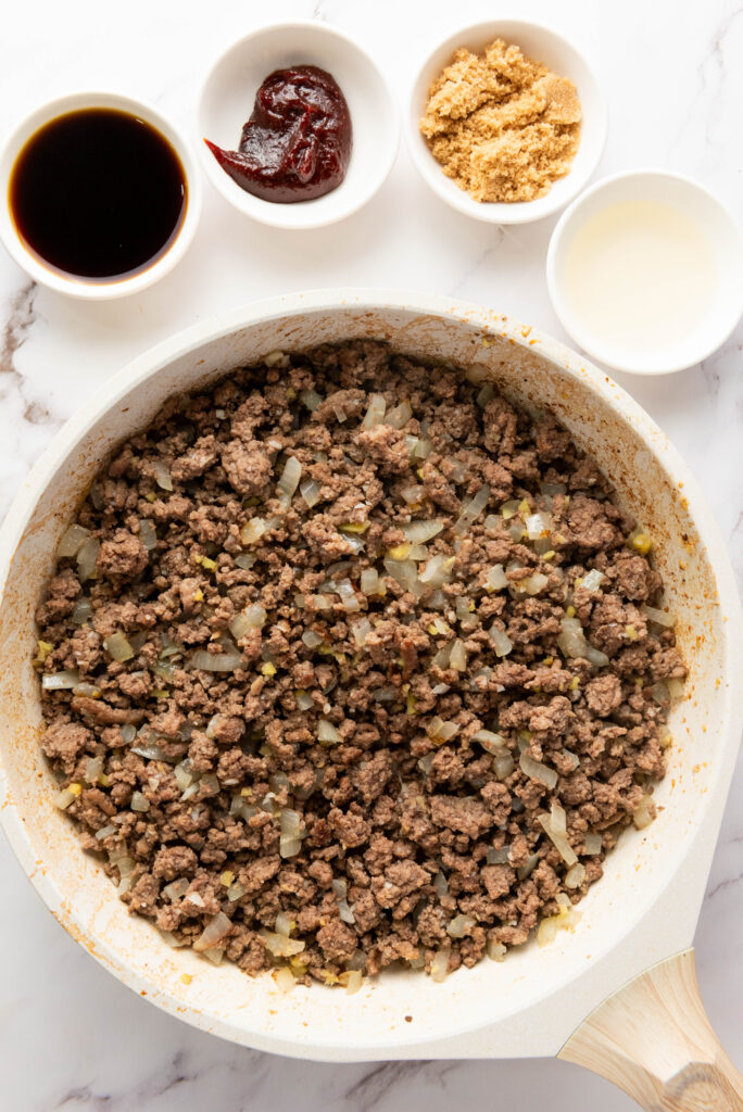A picture of ground beef, minced garlic, diced onion, and ginger cooked together in a skillet.