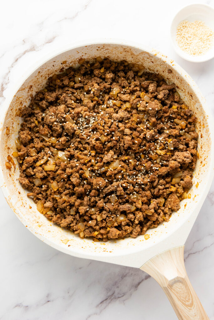 A picturere of a cooked ground beef mixture in a skillet, sprinkled with sesame seeds.