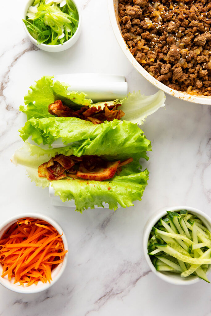 A picture of two butter lettuce leaves topped with kimchi.