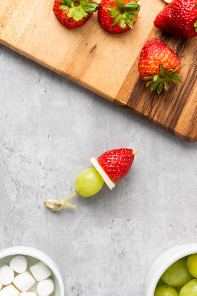 A picture of a grape, banana slice, and hulled strawberry threaded onto a skewer.