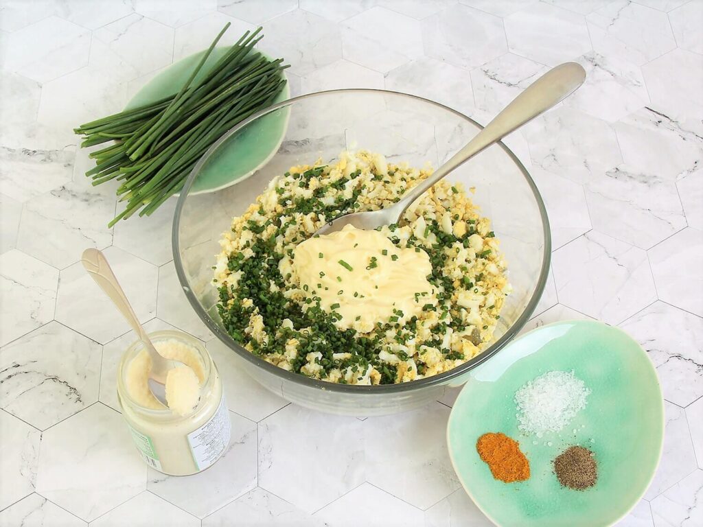 A picture of chopped eggs with chives, mayonnaise, and horseradish in a bowl, unmixed.