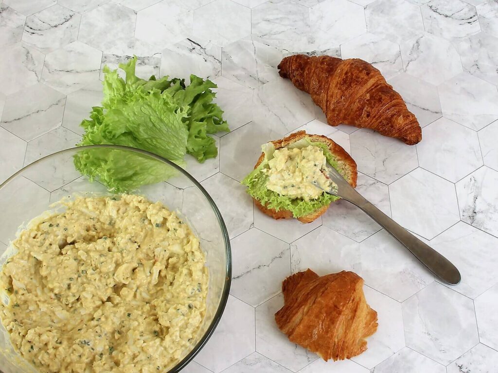 A picture of a croissant egg salad sandwich being constructed.