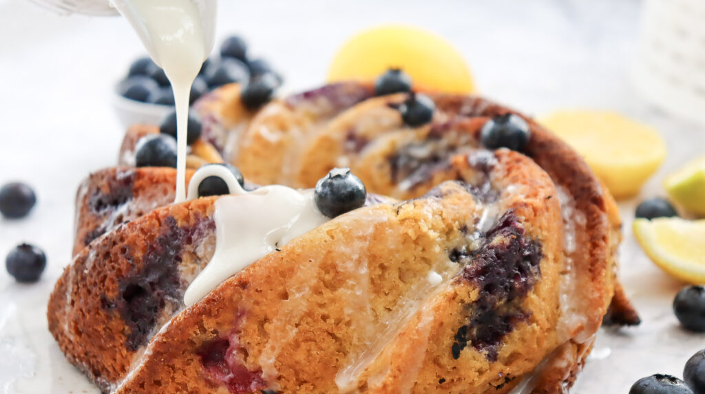 A picture of lemon blueberry bundt cake being drizzled with frosting.