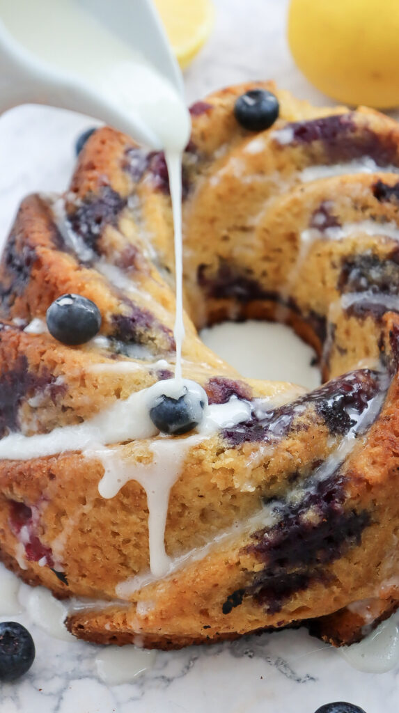 A picture of a lemon blueberry bundt cake being drizzled with frosting.