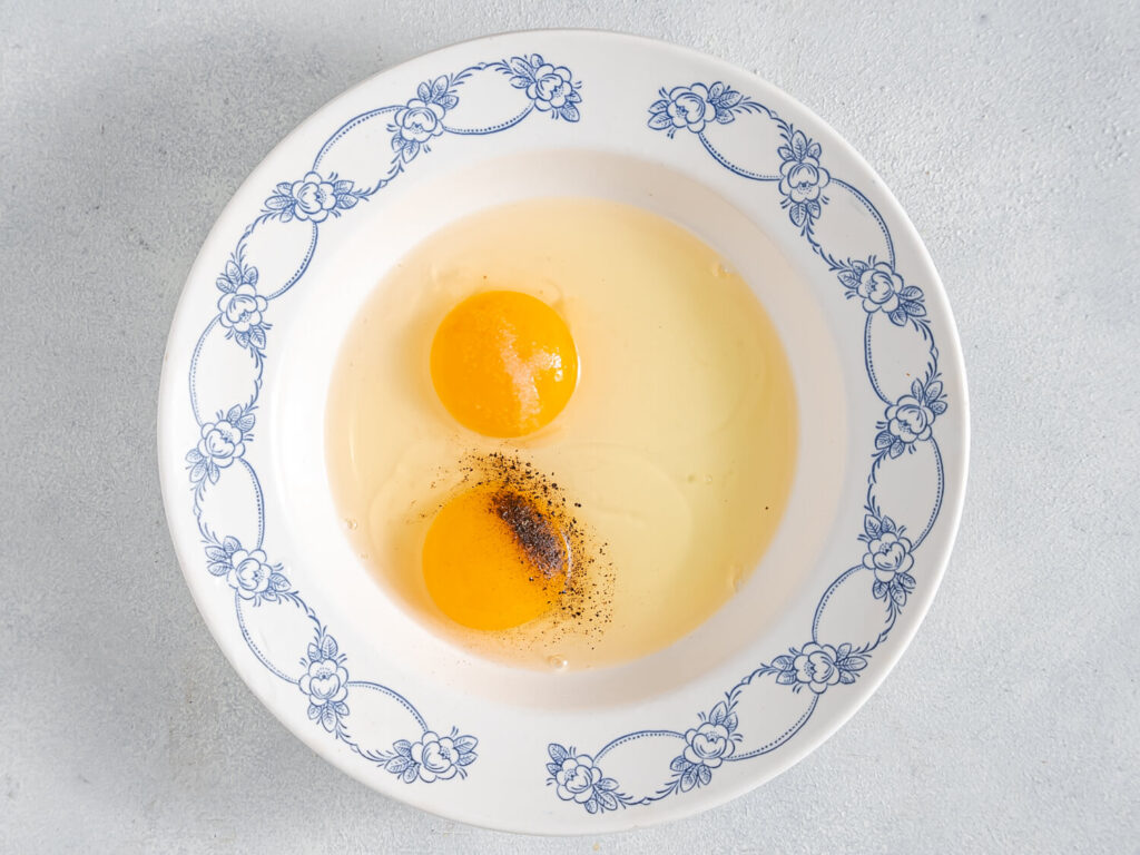 A picture of eggs in a bowl with salt and pepper.