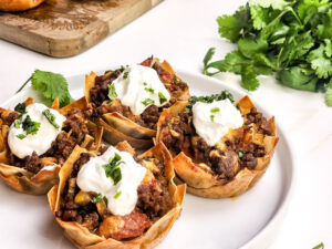 A picture of four mini taco cups with cilantro in the background.