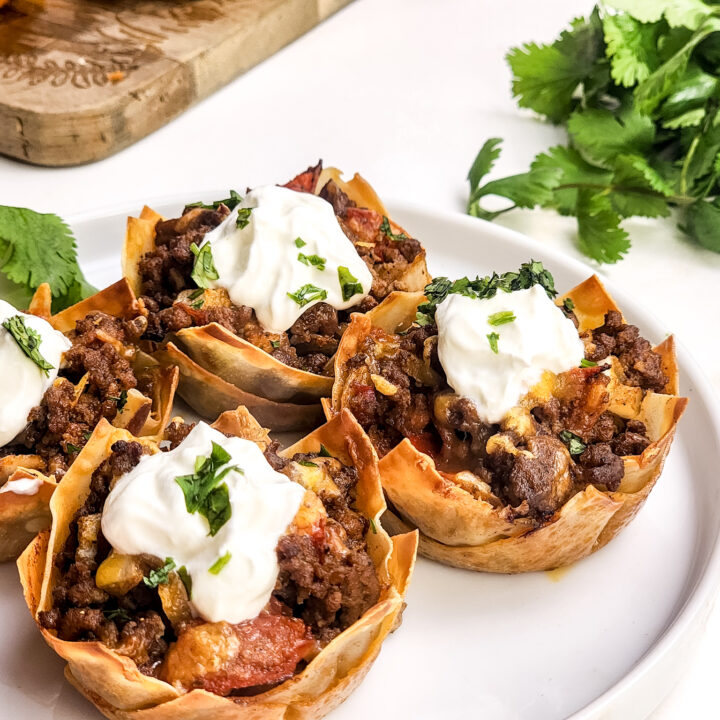 A picture of four mini taco cups with cilantro in the background.