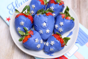 A picture of blue candy coated strawberries topped with silver candy stars on a plate.
