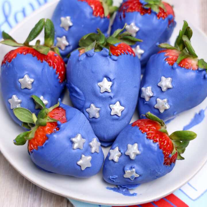 A picture of blue candy coated strawberries topped with silver candy stars on a plate.