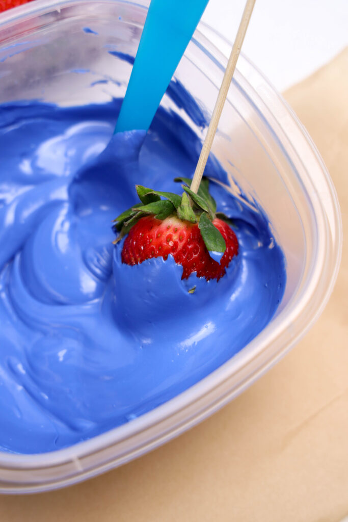 A picture of a skewered strawberry being dipped into melted blue candy.