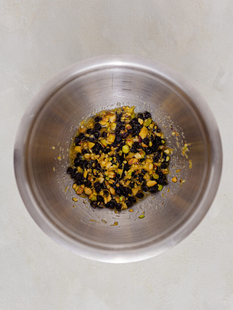 A picture of chopped pistachios, blackcurrants, lemon zest, olive oil and salt mixed together in a tin bowl.