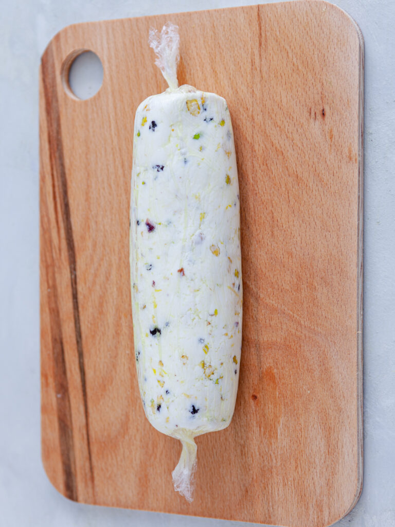 A picture of a cheese log rolled up in plastic wrap.