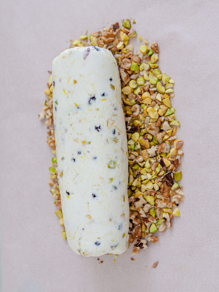 A picture of a cheese log on topo of a pistachio nut mixture.