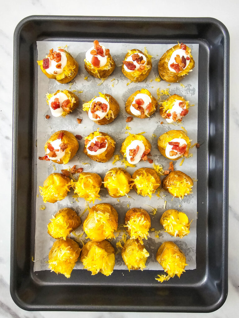 A picture of cooked mini potatoes topped with cheese, sour cream, and bacon.