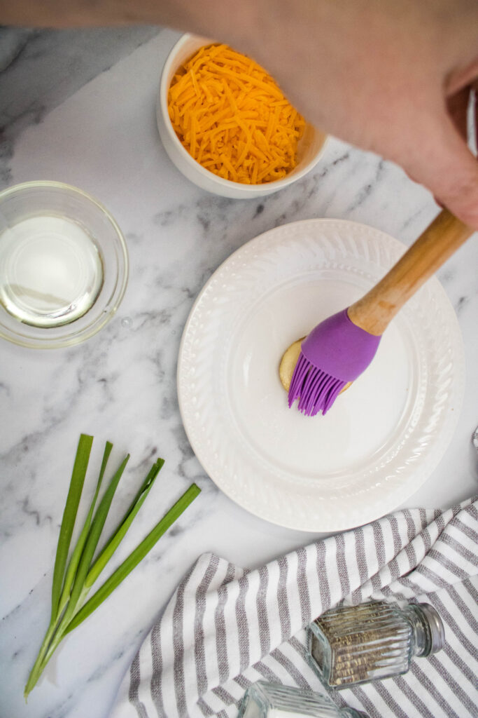 A picture of olive oil being brushed onto a potato slice.