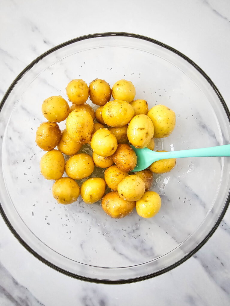 A picture of whole, raw potatoes mixed together with olive oil and sea salt.