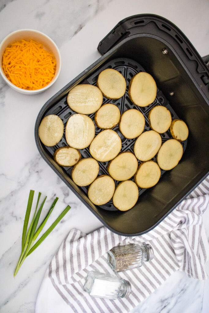 A picture of potato slices arranged in a single layer in an air fryer basket.
