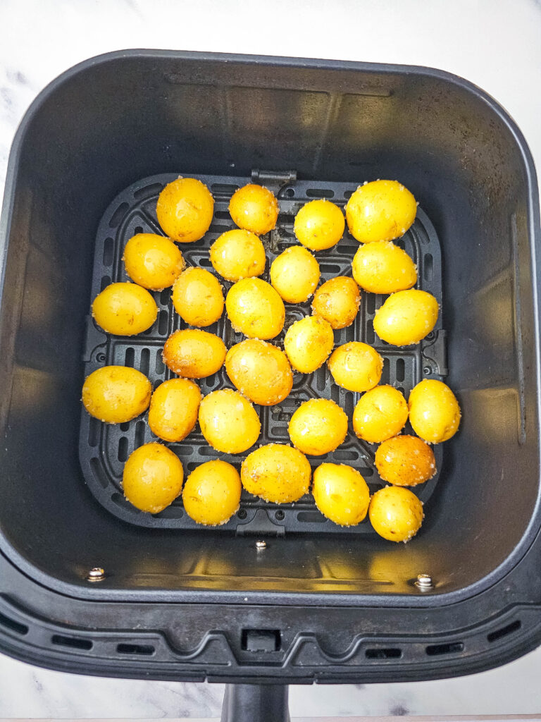 A picture of whole, raw mini potatoes coated with olive oil and sea salt in an air fryer basket.