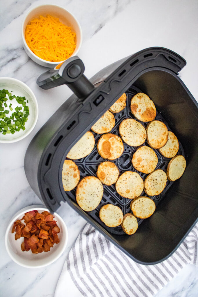 A picture of air fried potato slices arranged in a single layer in an air fryer basket.