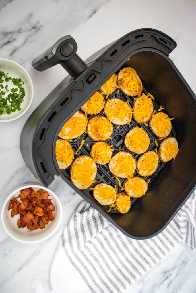 A picture of air fried potato slices topped with cheese, arranged in a single layer in an air fryer basket.