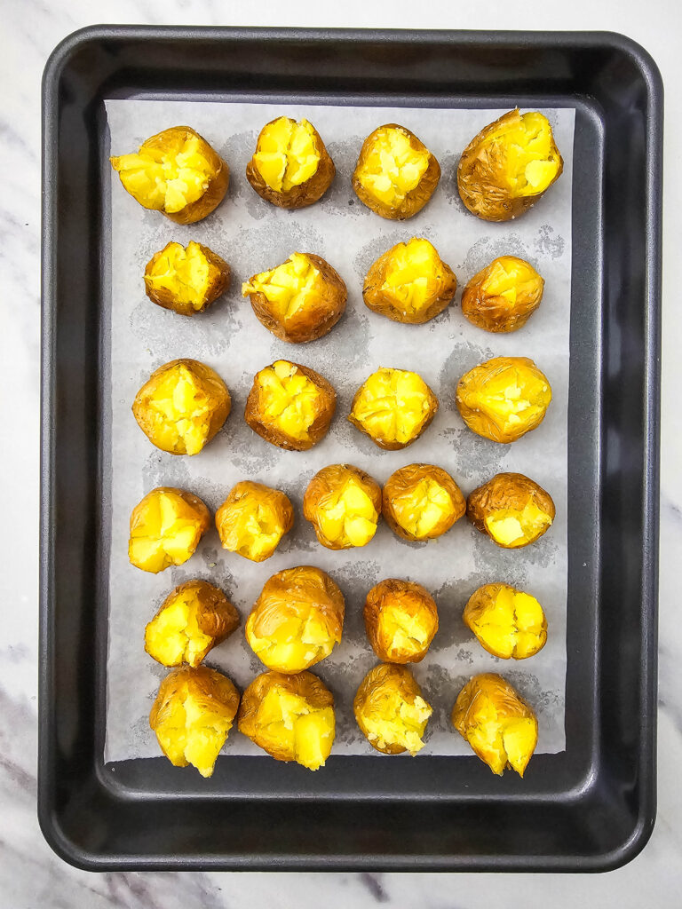 A picture of mini potatoes on a baking pan with the tops cut open.