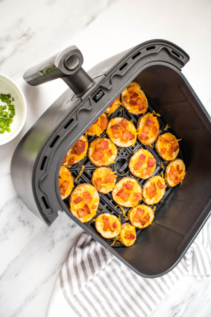 A picture of air fried potato slices topped with cheese and bacon, arranged in a single layer in an air fryer basket.