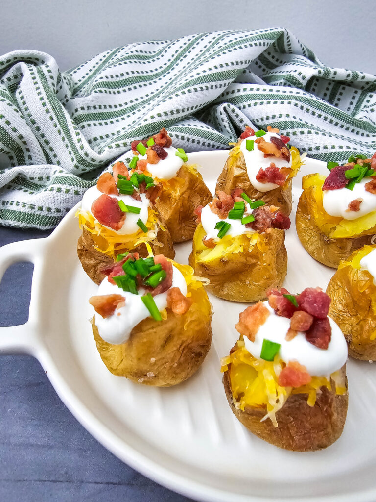 A zoomed in picture of mini loaded baked potato bites on a white platter.