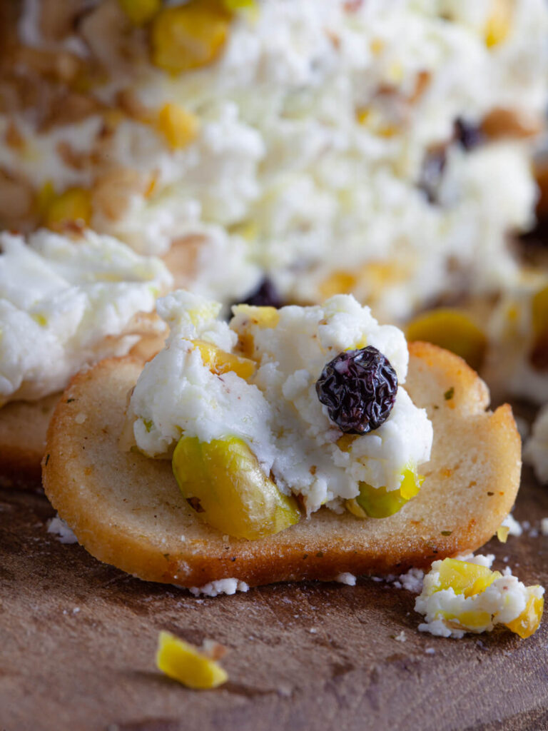 A picture of a cracker topped with pistachio and black currant cheese spread.
