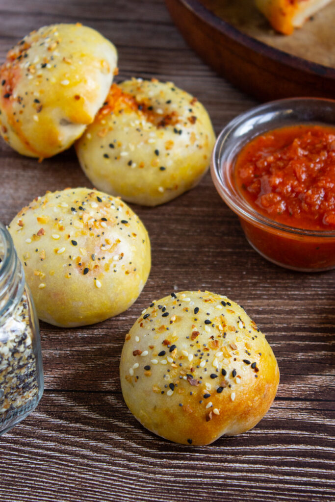 A picture of a set of baked pizza bagel bites on a wooden table with dipping suace nearby.