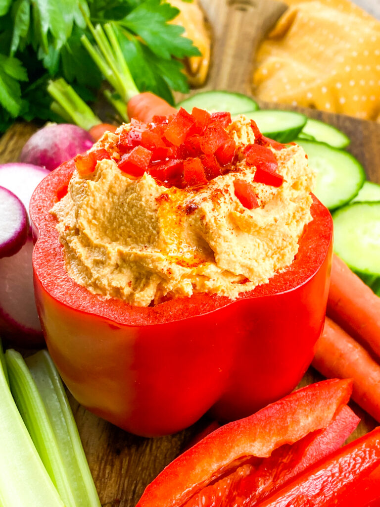 A picture of a red bell pepper stuffed with roasted hummus garnished with tomatoes.