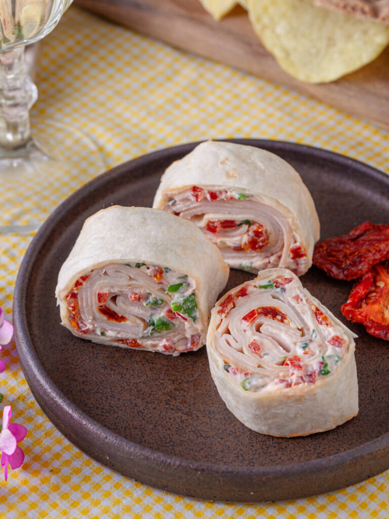 A picture of three turkey tomato pinwheel sandwiches displayed on a plate.