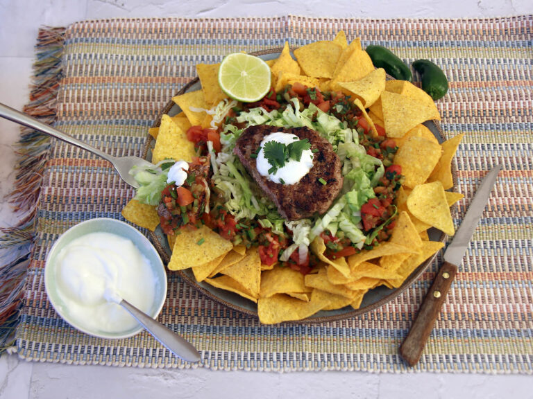 A picture of a burger with toppings on a bed of tortilla chips.
