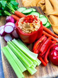 A picture of roasted red pepper hummus stuffing a red bell pepper with dippable vegetables around it.