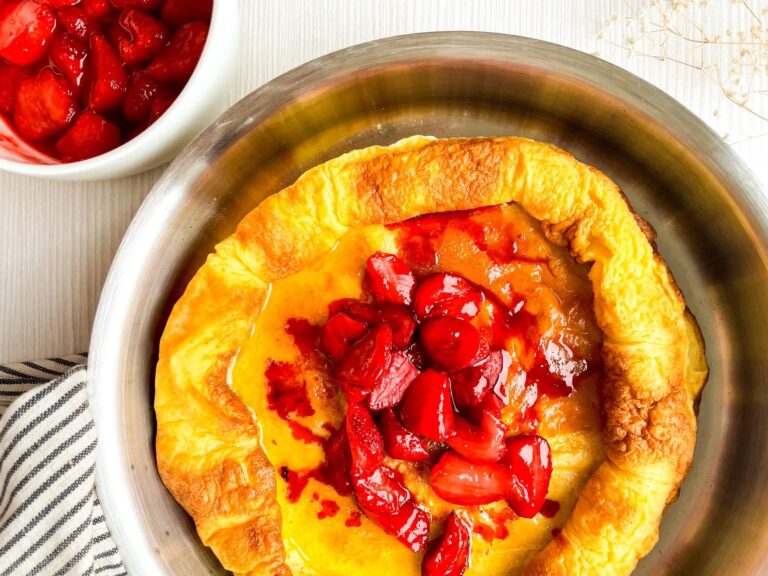 A picture of a roasted strawberry dutch baby with a bowl of roasted strawberries on the side.