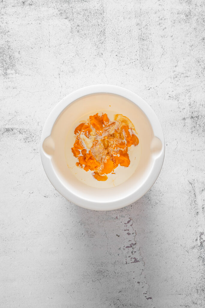 A picture of pumpkin puree, egg, cream, and vanilla extract unmixed in a bowl.