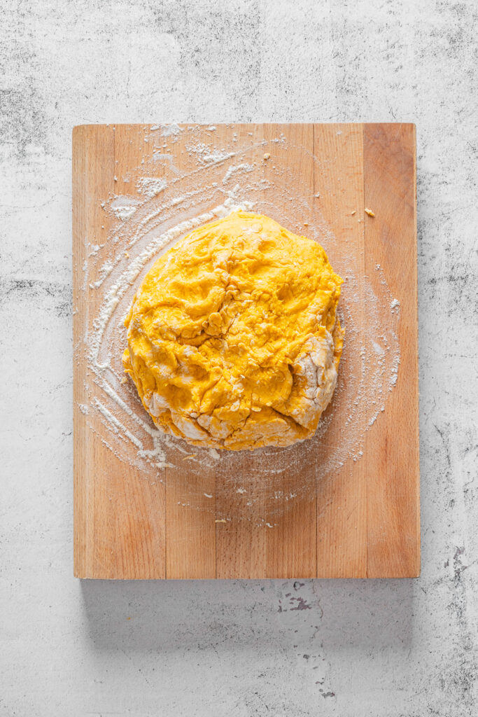 A picture of pumpkin spice scone dough dusted with flour on a wooden cutting board.