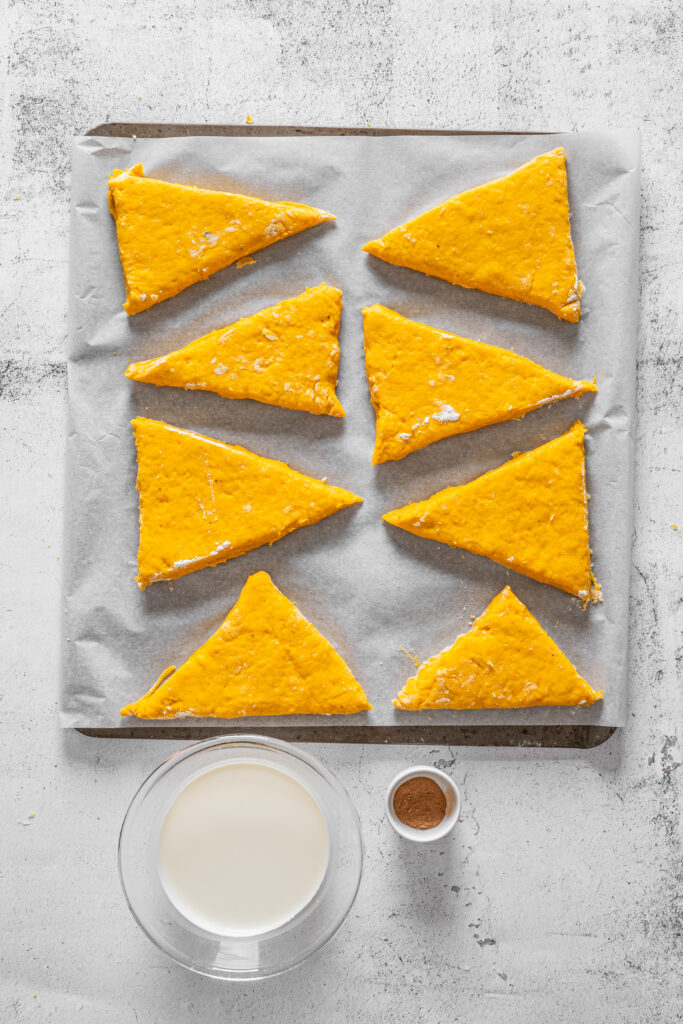 A picture of wedges of scone dough with cream and pumpkin pie spice in small bowls nearby.