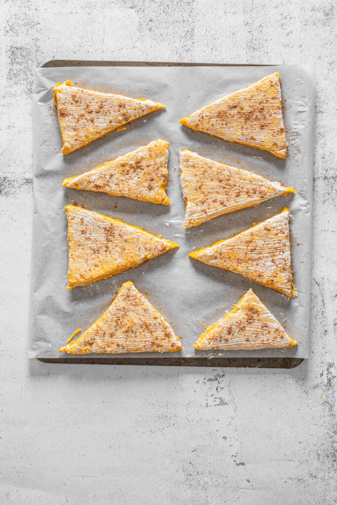 A picture of wedges of scone dough with cream and pumpkin pie spice brushed over the tops.