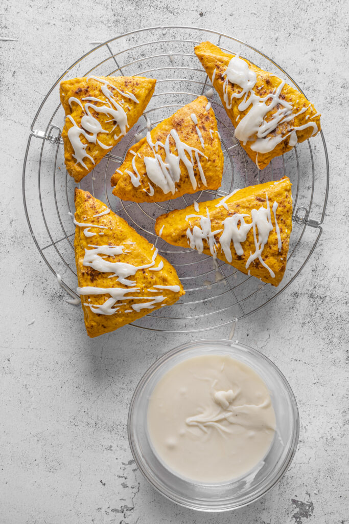 A picture of pumpkin pie scones drizzled with cream glaze on a wire rack.