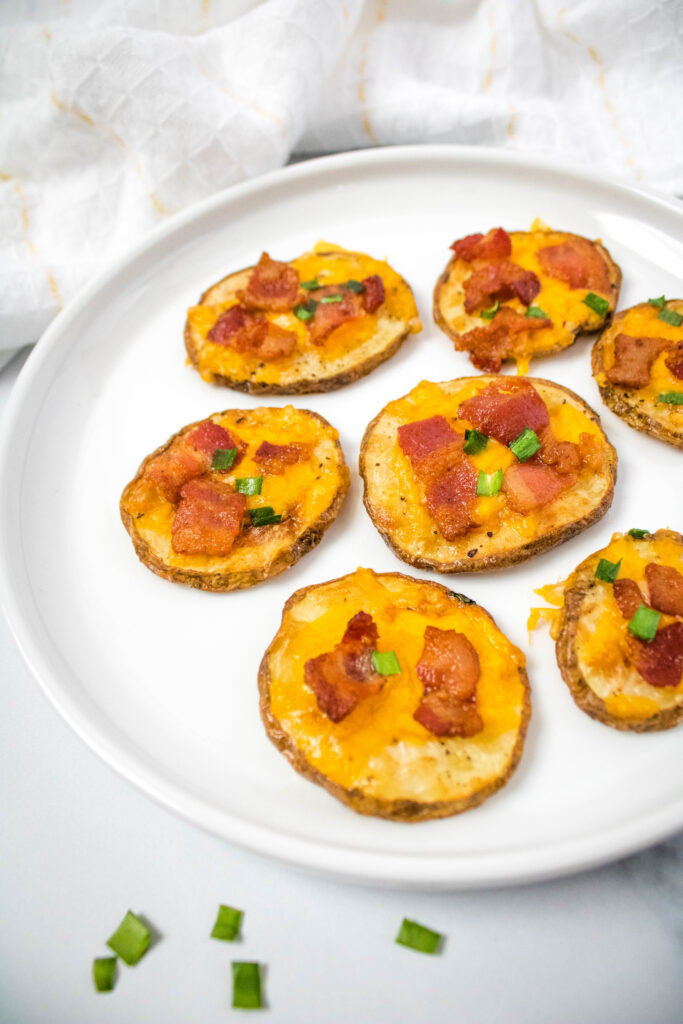 A zoomed in picture of fully cooked bacon and cheese potato slices on a white plate.