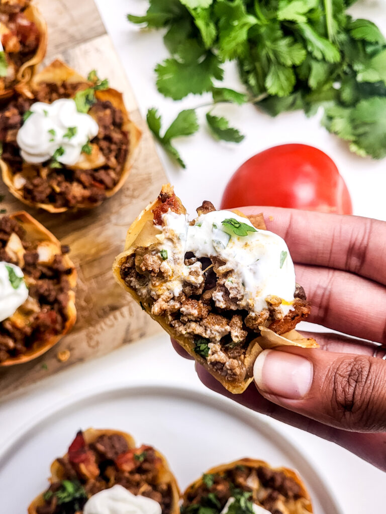 A picture of a hand holding a mini taco cup with a bite taken out of it.