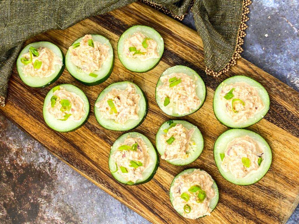 A picture of cucumbers covered with spicy tuna on a wooden platter.