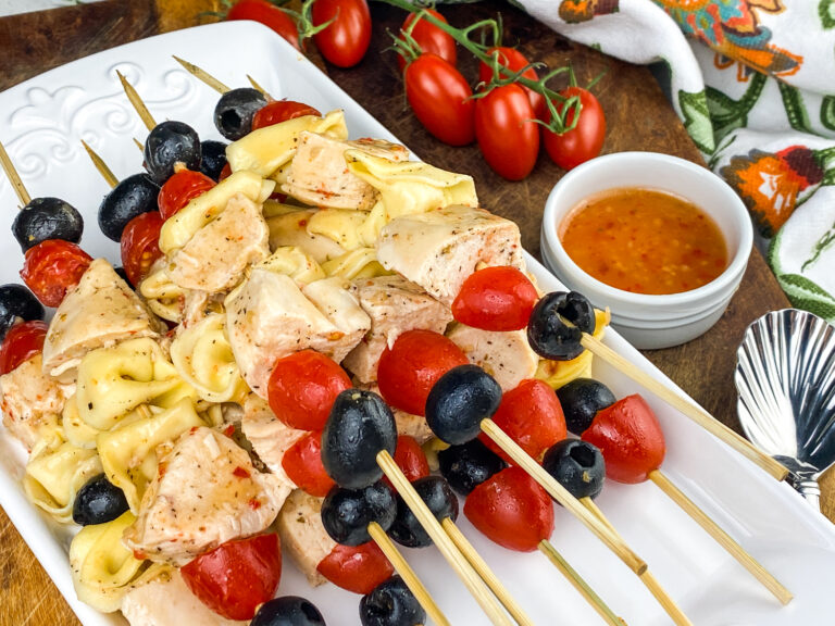 A picture of a platter of chicken and tortellini skewers with olives and tomatoes.